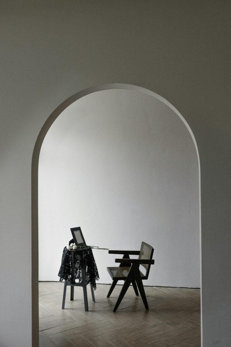Serene minimalist room with a wooden chair and table through an archway.